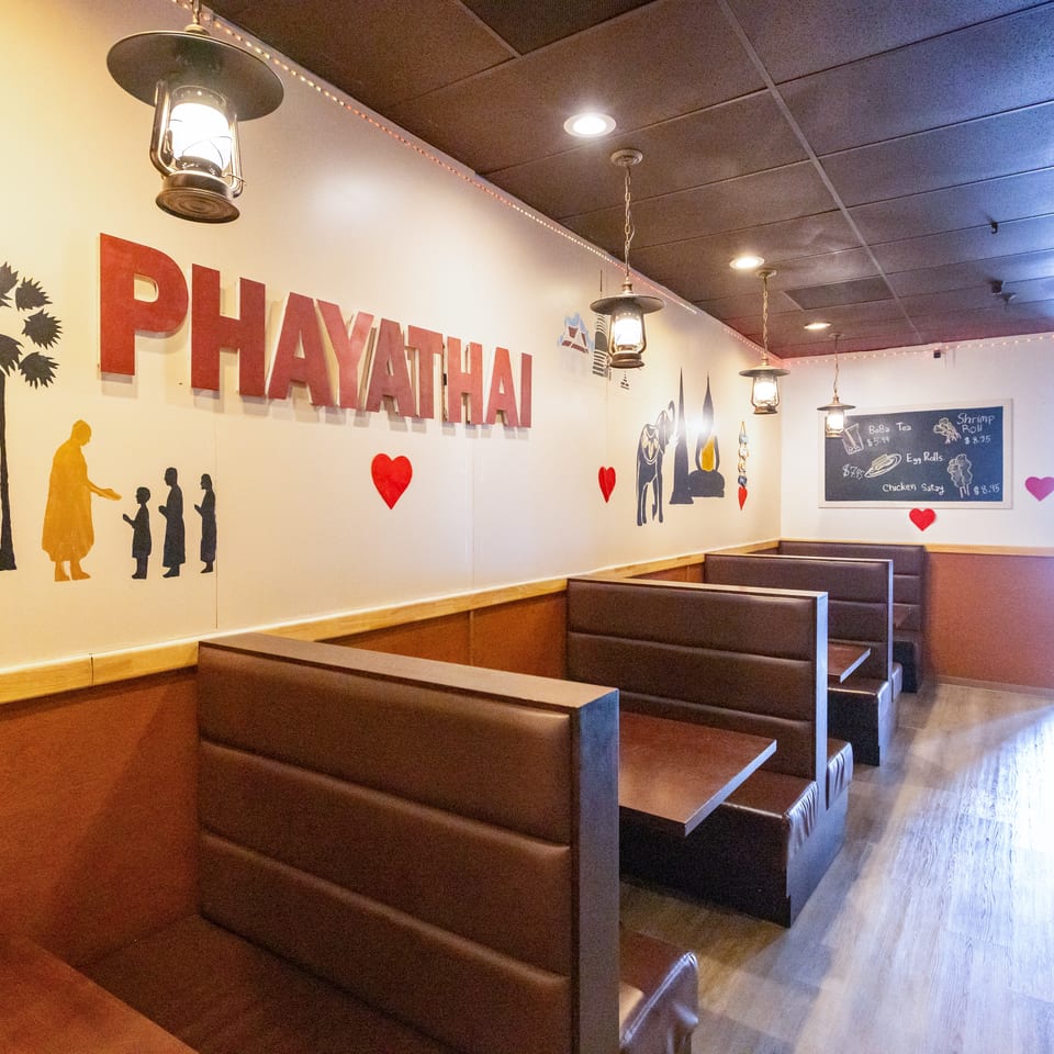 Thai restaurant interior with booth seating, lantern-style lights, colorful wall murals, and a chalkboard menu.