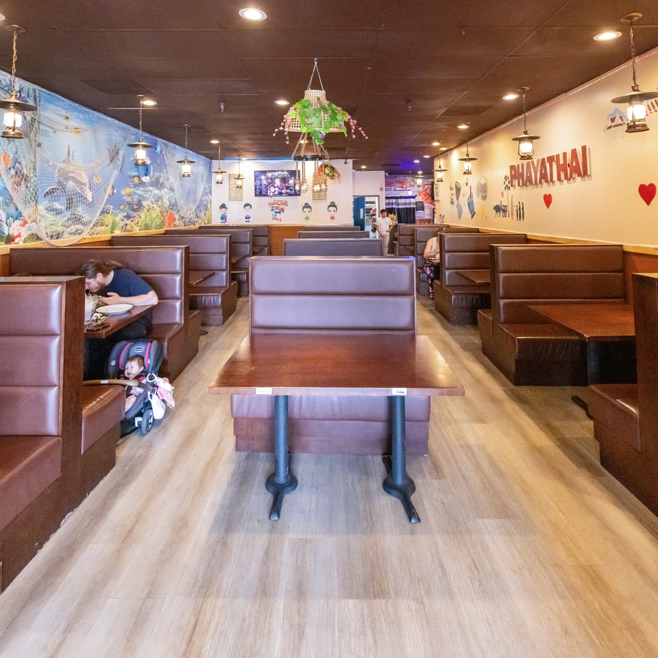 Thai restaurant dining room with leather booths, ocean-themed mural, hanging lanterns, Thai artwork, and several diners.